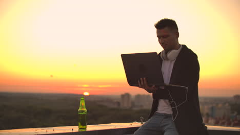 Hipster-man-with-a-laptop-on-the-edge-of-the-roof.-Freelancer-at-work.-Wireless-mobile-Internet.-He-works-on-the-Internet.